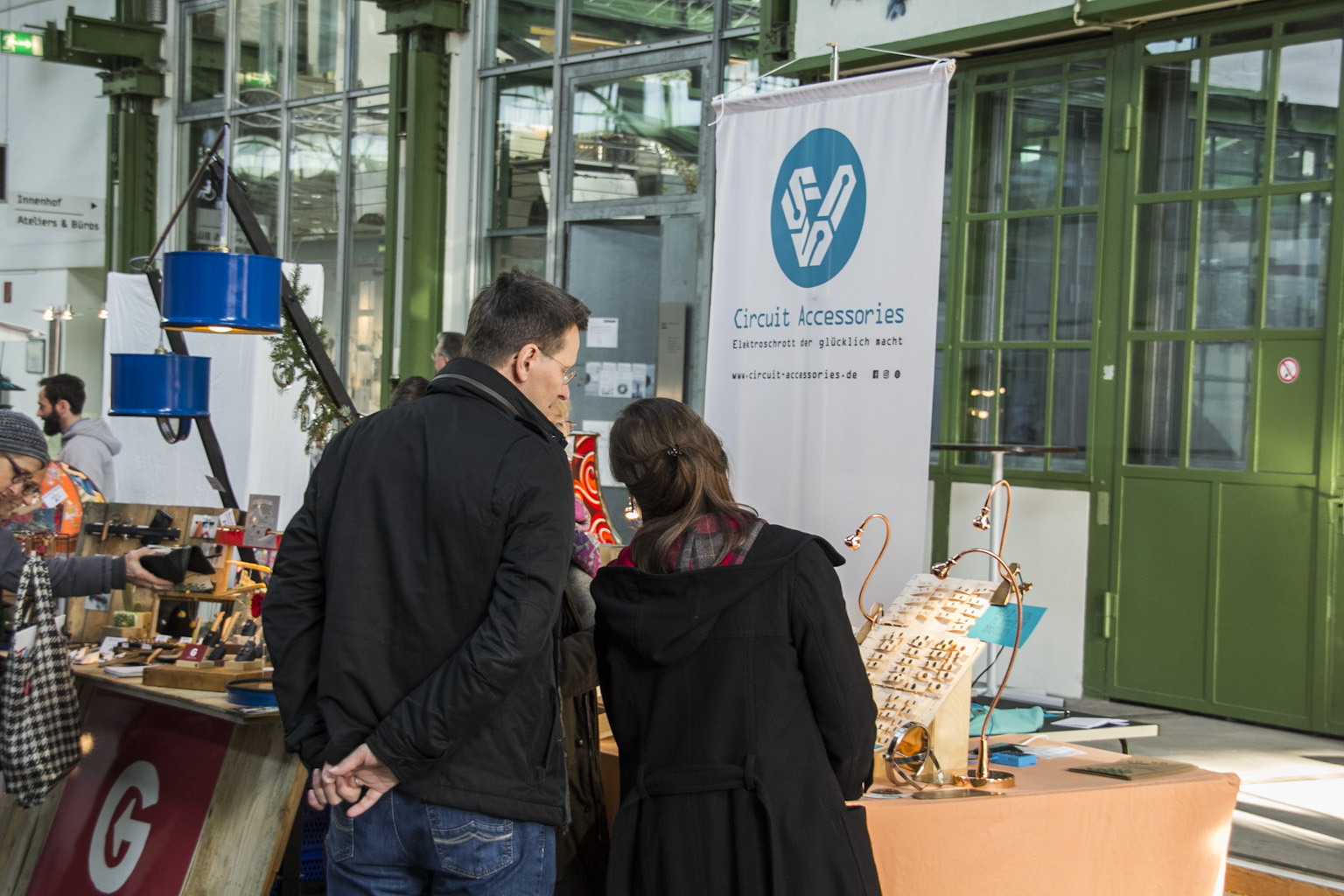 Zwei Personen betrachten an einem Messestand die Ausstellung von Circuit Accessories in einer Industriehalle.