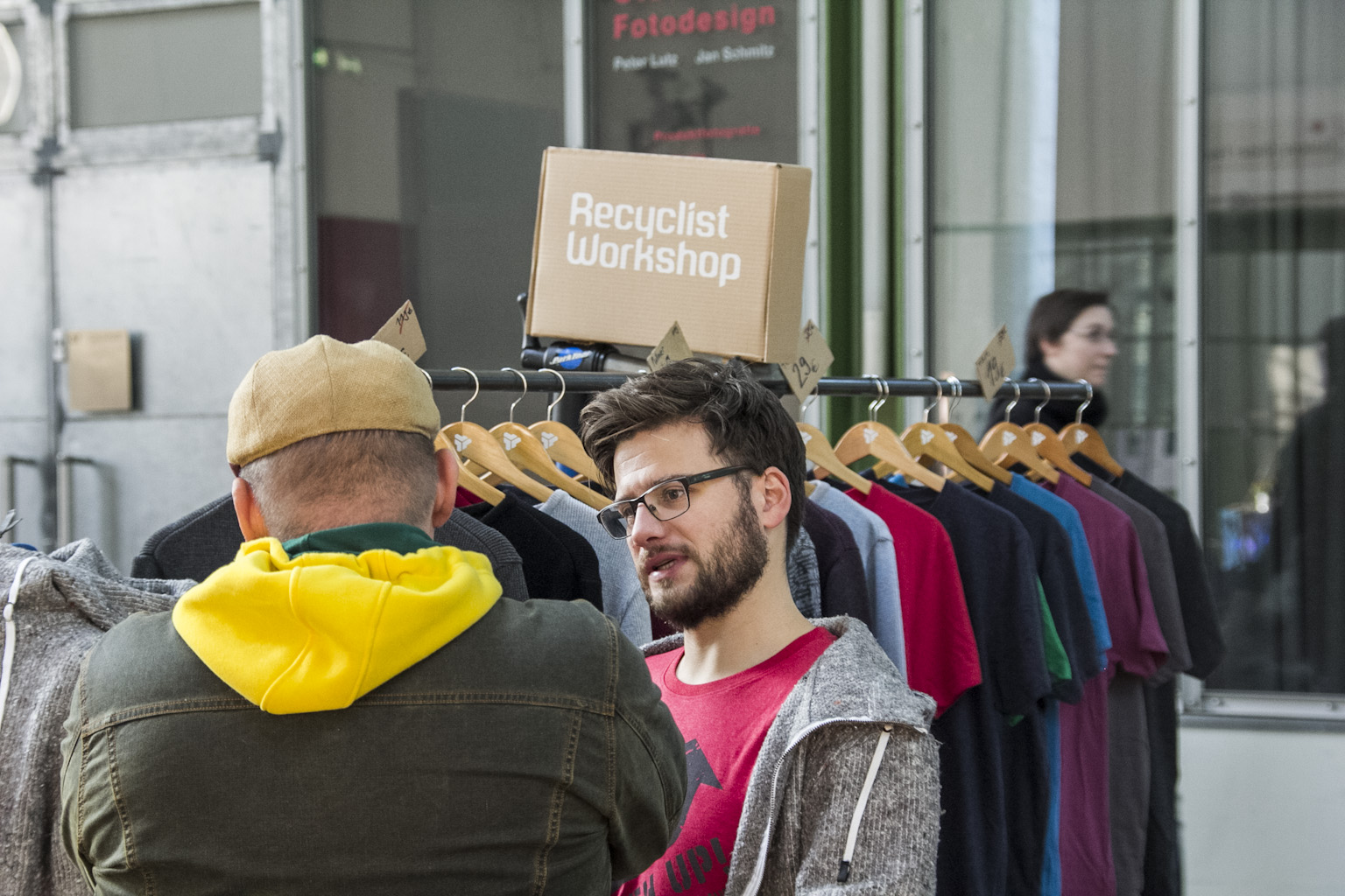 Besucher einer Recyclist Workshop betrachten Second-Hand-Kleidung an Kleiderstangen.