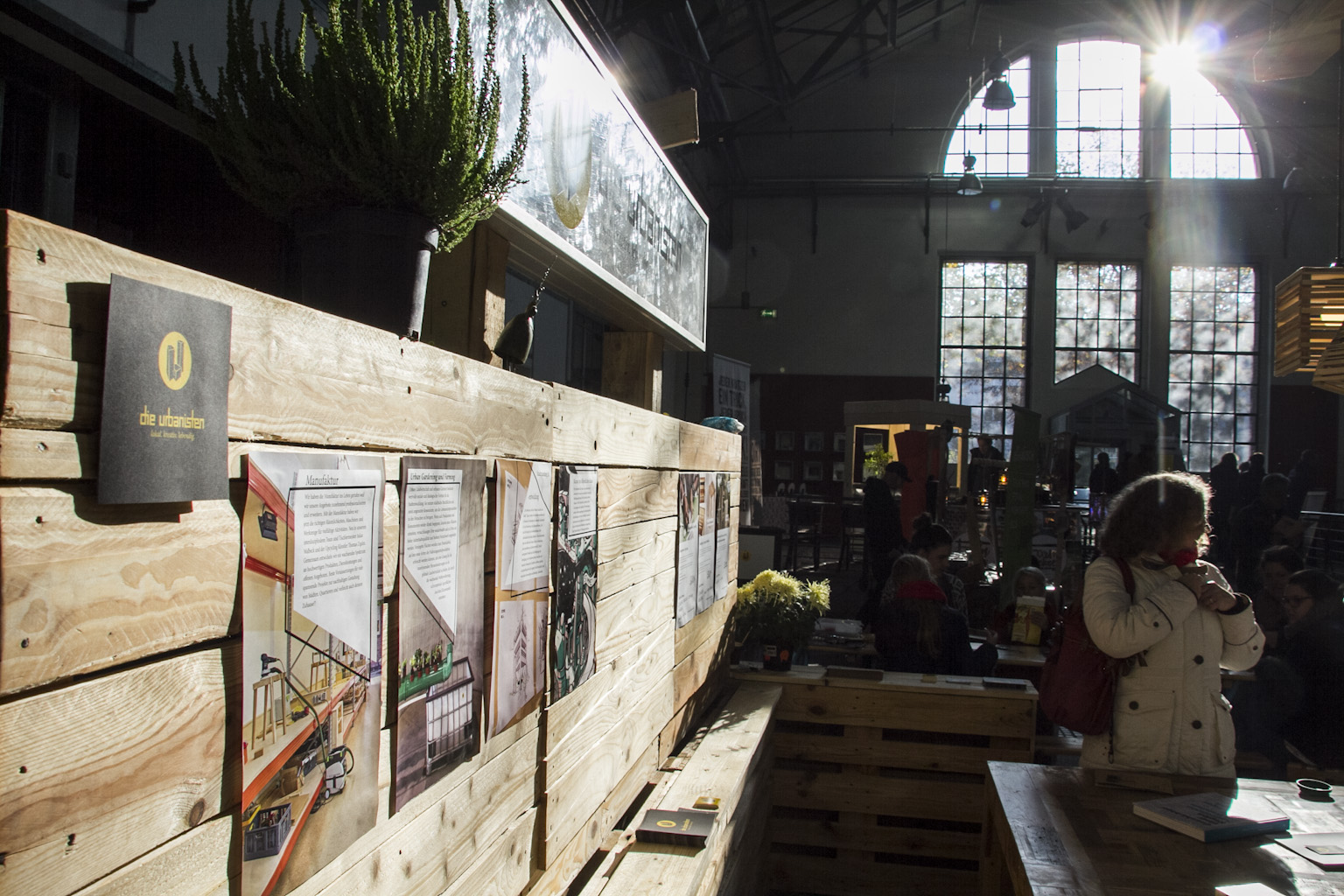 Holzkonstruktion mit Informationstafeln und Fotografien zur Stadtentwicklung in einer Industriehalle.