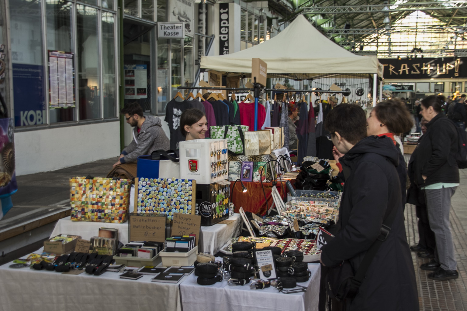 Markstand mit Kunsthandwerk und Kleidung auf Dortmunder Markt unter Zelt, Besucher schauen sich Waren an.