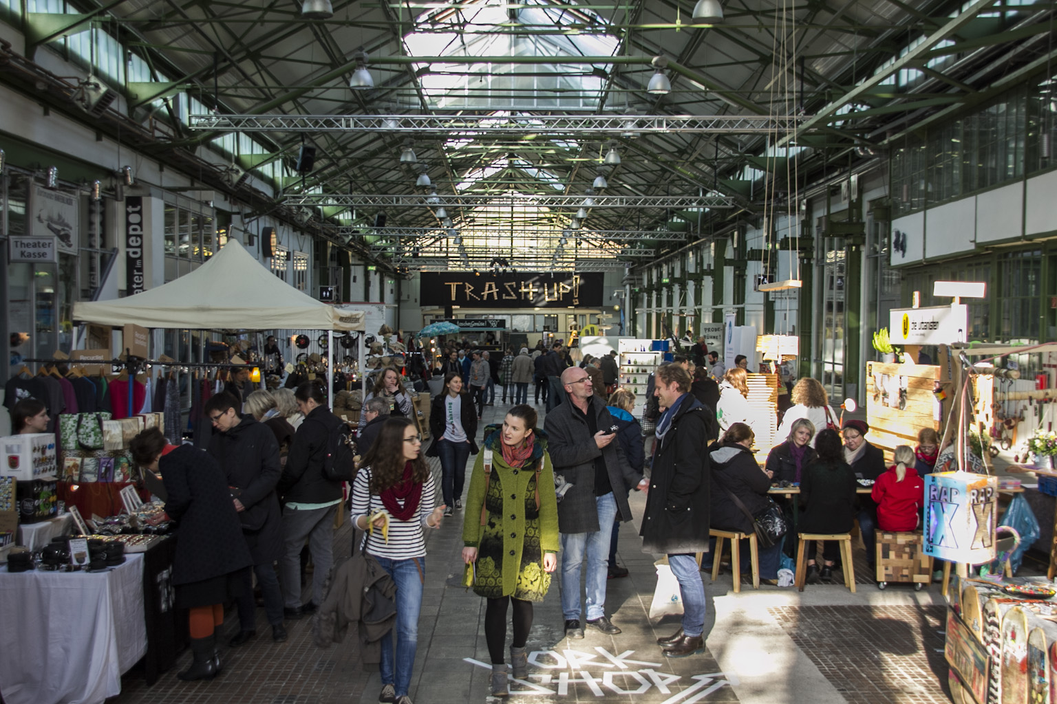 Großes Innenfest in einer Industriehalle mit vielen Besuchern, Marktständen und buntem Programm.