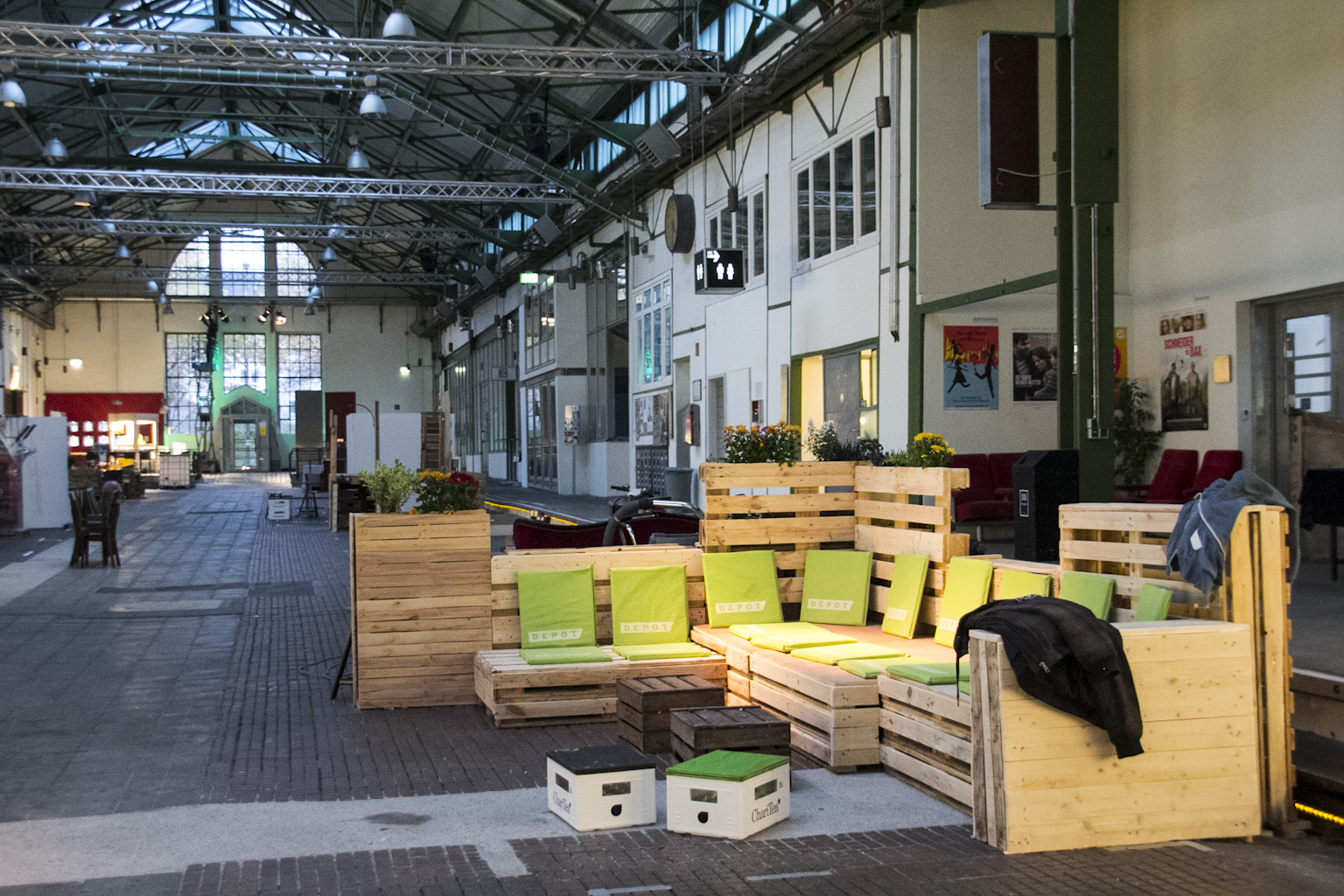 Umgebauter Industrieraum mit Sitzbereichen aus Holzpaletten und grünen Polstern.